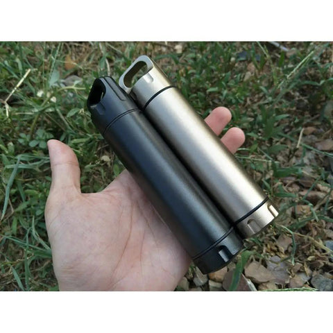 Hand holding two Portable Survival Waterproof Pill Container For Outdoor EDC Gear, CNC Machined Aluminum Bottles, shown in silver and black.
