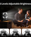 Camping Fan With Light 20000mAh Rechargeable Battery illuminating a couple by the campfire with adjustable brightness settings.