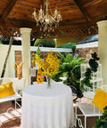 Plug-In Five Light Crystal Chandelier Swag Hanging Fixture With White Metal Frame And Clear Glass Stems And Acrylic Crystals Ideal For Nurseries Bedrooms Bathrooms Closets Hallways And Events hanging in outdoor gazebo over a table with yellow flowers.