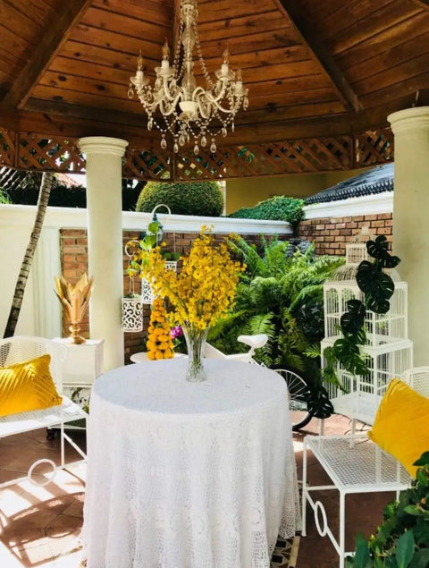 Plug-In Five Light Crystal Chandelier Swag Hanging Fixture With White Metal Frame And Clear Glass Stems And Acrylic Crystals Ideal For Nurseries Bedrooms Bathrooms Closets Hallways And Events hanging in outdoor gazebo over a table with yellow flowers.