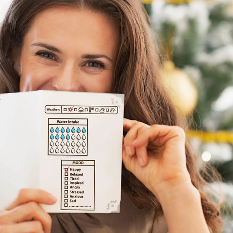 Woman holding a journal page featuring water intake and mood tracking for her daily journaling setup.