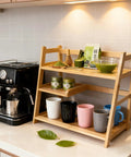 Bamboo Matcha Station Organizer with 3-Tier Shelf beside espresso machine, holding tea accessories and mugs in kitchen setting.