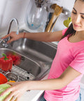Woman washing vegetables over Heavy Duty Sink Grid 26-Inch By 14-Inch Stainless Steel Kitchen Protector Rack in use
