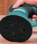 Person using five inch round backing pad with hook and loop for quick paper changes, eight hole design for easy dust extraction.