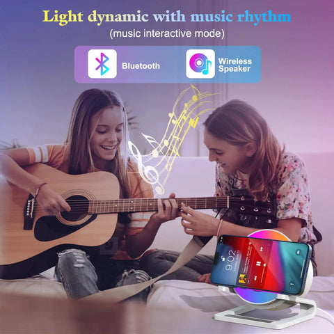 Girls playing guitar and smiling next to 4 In 1 Night Light Bluetooth Speaker With Wireless Charging 15W, phone on stand