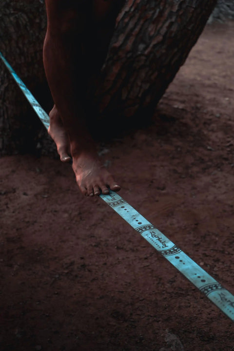 Close-up of feet balancing on a 60 Feet Slackline Kit With Tree Guards, Carry Bag, And Easy Setup For Family Fun, Kids And Adults