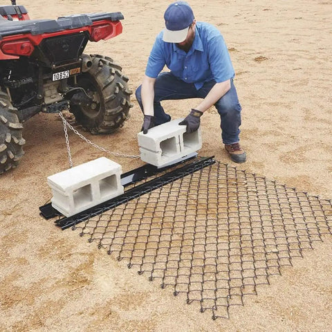 Heavy Duty Steel Drag Harrow And Field Leveler For ATV UTV And Tractor With Front Tray 5 By 4 Feet Keeps Soil Even For Lawn Farm And Landscape Prep For Soil Leveling And Dirt Moving On Fields Or Driveways, Easy To Attach And Use setup by a person hooking it to an ATV on a sandy field.