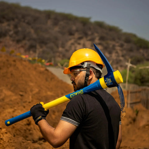 Worker holding a Heavy Duty 5-Pound Pick Mattock With 36-Inch Fiberglass Handle, Drop-Forged Heat-Treated Head for Breaking Hard Ground