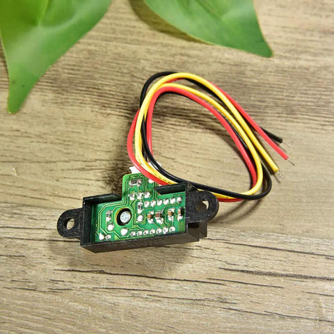 Sharp IR Analog Distance Sensor GP2Y0A21YK0F with wires shown on a wooden surface used in Arduino projects and robotics.
