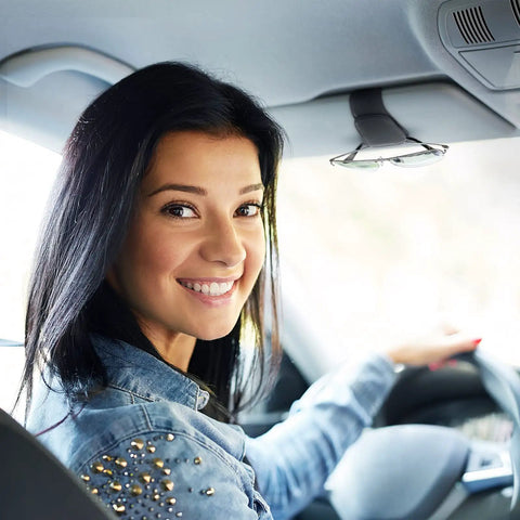 Smiling woman driving a car with a Heavy Duty Magnetic Sunglass Holder For Car Sun Visor With Secure Snap Clip and Soft Leather Wrap.
