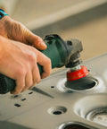 Green angle grinder with red grinding wheel, close-up view on metal surface.