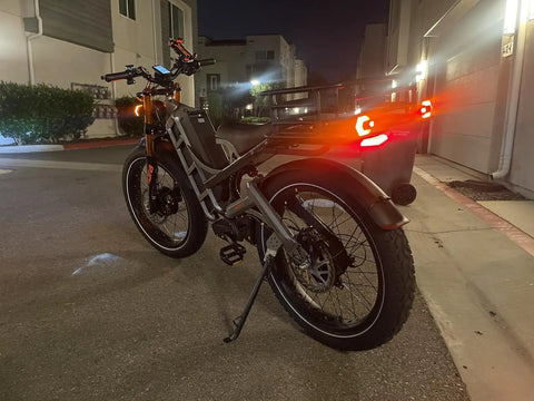 Romeo Pro Electric Bike With 5600W Dual Motors Hitting Fifty Mph Shredding Gnarly Dirt Paths Using Sixty Volt Eighty Amp Hours Cells Yielding Two Hundred Fifty Miles Across Chunky Four Point Zero Foot Tires And Rigid Rear Cargo Bags in urban setting at night.