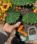 Mystic Gnome Fairy House Solar Light for Outdoor Decor held by a hand, with flowers background, 12in H polyresin lantern.