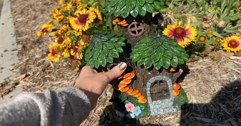 Mystic Gnome Fairy House Solar Light for Outdoor Decor held by a hand, with flowers background, 12in H polyresin lantern.