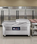 Chamber Vacuum Sealer With 1200 Watts And A Generous 23 Inch Seal Bar in a professional kitchen setting with stainless steel fridges.
