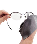 Microfiber cleaning cloth wiping metal-frame eyeglasses; gray, close-up