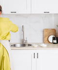 Person in yellow reaches over sink with Oil Rubbed Bronze Curved Cabinet Handles Arch Drawer Pulls visible on white cabinets.