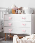 White dresser with Pink Bow Dresser Knob Set With 30 Knobs And 90 Screws, 1.57 Inch Aluminum Alloy Handles adorning drawers.