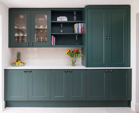 Modern kitchen with dark green cupboards featuring glass doors, books, and decor on shelves.