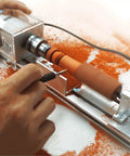 Close view of Compact Mini Lathe Machine For Metal Turning And Woodworking shaping a wood piece with orange shavings.
