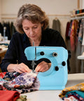 Woman using Get Your Threads Sorted Quick Super Portable Sewing Machine For Beginners on colorful fabrics at a sewing station.