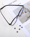 Eyeglass Repair Kit With 6 Pairs Silicone Grips Hinge Rings And Temple Tighteners Plus 3 In 1 Screwdriver For Glass Frames, showing black eyeglasses with silicone rings next to a magazine on a table.