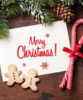 Festive Christmas scene with Merry Christmas card, candy canes, gingerbread cookies, and pine branches on rustic wood background.
