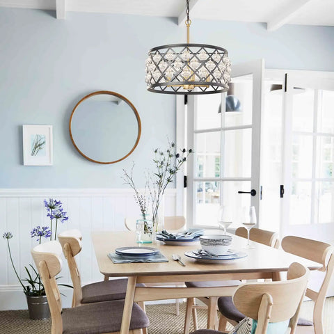 Matte black and gold crystal chandelier hanging above dining table with chairs, creating an elegant focal point in a bright room.