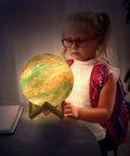 Child admiring the 7.0 Inch Moon Lamp Night Light with 16 Color LED, 3D Printed Moon Surface, on wooden stand.