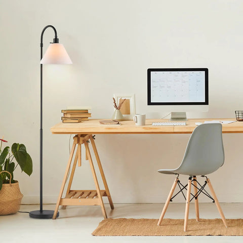 Barden 58 Inch Floor Lamp In Dark Bronze With Beige Fabric Shade beside a wooden desk and chair in a minimalistic room.