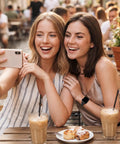 Two women smiling while taking a selfie, featuring a smart watch on one wrist, enjoying drinks and pastries outdoors.