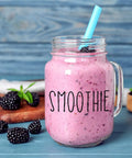 Glass jar with blackberry smoothie and straw, surrounded by fresh blackberries on wooden cutting board with the word 'SMOOTHIE' on the jar.