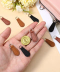 Hand holding PU leather zipper pull tabs in black, khaki, red-brown from the Zipper Pull Tabs Replacement Kit for Luggage Backpacks Jackets Purses And Handbags Grab And Go Easy Clip On PU Leather Zipper Pulls No Tools Required 12 Pack In Black Khaki And Red Brown Perfect Fixes For Broken Zippers.