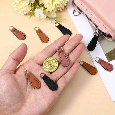 Hand holding PU leather zipper pull tabs in black, khaki, red-brown from the Zipper Pull Tabs Replacement Kit for Luggage Backpacks Jackets Purses And Handbags Grab And Go Easy Clip On PU Leather Zipper Pulls No Tools Required 12 Pack In Black Khaki And Red Brown Perfect Fixes For Broken Zippers.