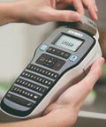 Badass Portable Label Maker Featuring Authentic Qwerty Keyboard And Rapid Response Touch Keys with printed label in hand.