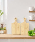 Two bamboo cutting boards with handles shown in front view on a wooden kitchen counter, 11x5 inches.