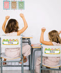 Two children sitting at desks with 50 Pack Hot Air Balloon Style Desk Nameplates For Students on chair backs, bright classroom decor.