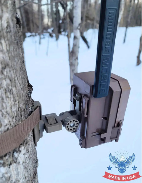 Versatile Trail Camera Mount For Moultrie Edge Models 2 And 3 Solar on tree with strap in snowy forest.