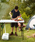 Person using Portable Outdoor Fish Cleaning Table with Sink and Sprayer, folding design with steel frame at campsite