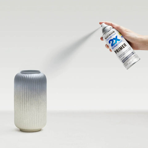Pro Grade Painter Touch Spray Primer In Flat Gray Six Pack Of Twelve Oz Cans For Wood Metal And Plastic With Fast Dry Formula And Zero Hassle Any Angle Grip Application, spray can in hand above a textured vase.