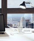 Desk with laptop, lamp, glasses, and a to-do list against city skyline view