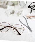 Stainless Steel Two Piece Eyeglass Repair Kit With Flat Nose Pliers And Precision Screwdriver For Quick Adjustments, Nose Pad Pliers, And Glasses Repairs On The Go on display with eyeglasses and repair tools.
