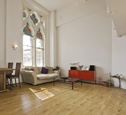Modern living room with large stained glass windows featuring a colorful pattern, wooden flooring, and contemporary furniture.