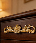 Upgrade Your Furniture Game Now With These Hella Charming Golden Floral Cabinet Handles And Vintage Drawer Pulls Designed To Bring Major Retro Swagger To Dresser Drawers And Bedroom Wardrobe Cabinetry Projects Instantly, close-up view of gold floral handle on dark wood drawer.