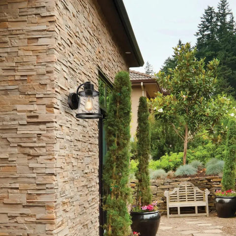 Oil Rubbed Bronze Outdoor Indoor Wall Sconce With Seeded Glass Shade installed on stone wall in rustic garden patio setting.