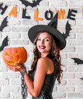 Woman in witch costume holding Halloween pumpkin with black plastic wrist shackles handcuffs with chain links for cosplay.
