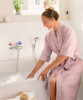 Woman in pink robe using a bathtub faucet with 6 Pack Hella Durable Hot And Cold Water Faucet Labels Self Adhesive Waterproof Sink Temperature Stickers.