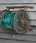 NeverLeak Decorative Wall Mount Hose Reel In Brown For Outdoor Yards Holds 125 Ft Of Five Eighths Inch Hose With Durable Corrosion Resistant Metal Construction And Included Leader Hose For A Leak Free Easy Hose Storage Station mounted on wall.