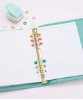 Planner with decorative hole reinforcers punch for planners and tags, adhesive circle hole punch tool in use, multi-color circles, open planner