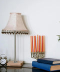 Decorative lamp, clock, and candle holder on a shelf with books in a home setting